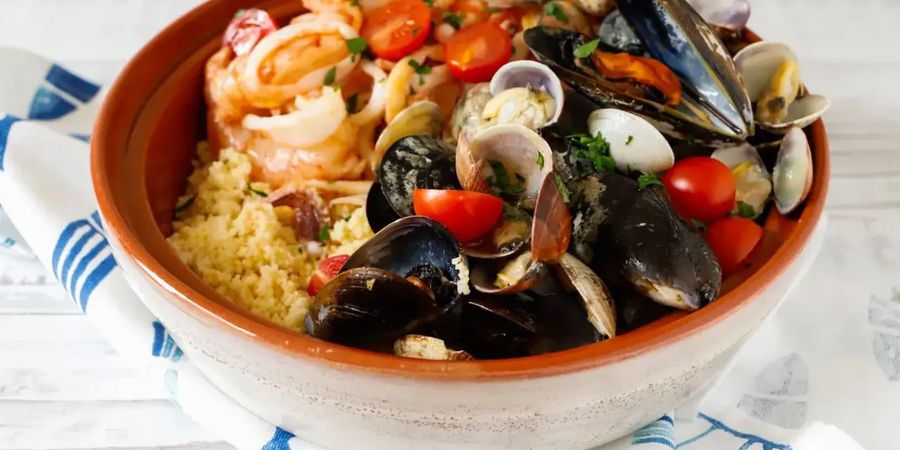 Un invitante cous cous di pesce, ricco di cozze, vongole, gamberi e pomodorini, guarnito con prezzemolo fresco.