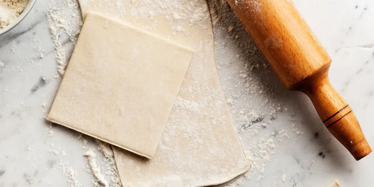 Farinata e mattarello su piano di marmo, pronti per creare pasta sfoglia fatta in casa.