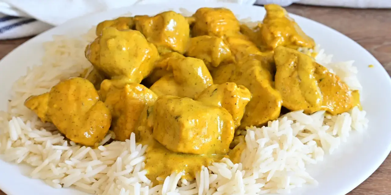 Piatto di riso basmati con saporito pollo al curry, ricoperto da una cremosa salsa gialla.