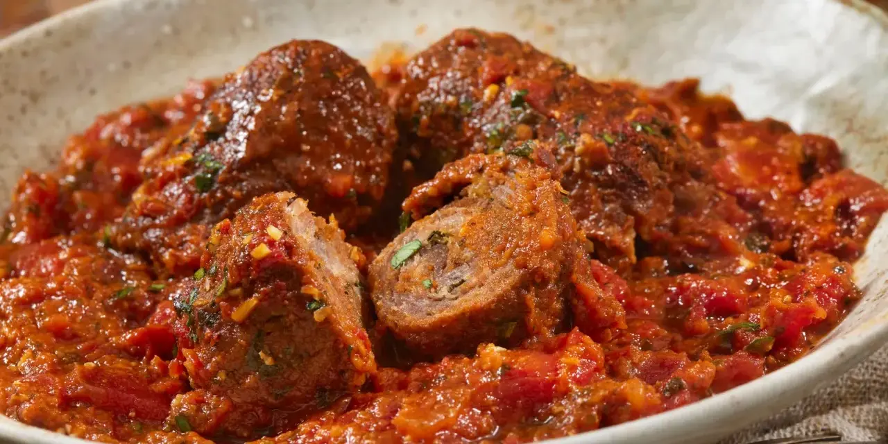 Involtini alla romana succulenti in un ricco sugo di pomodoro, con un interno visibile che rivela erbe aromatiche.