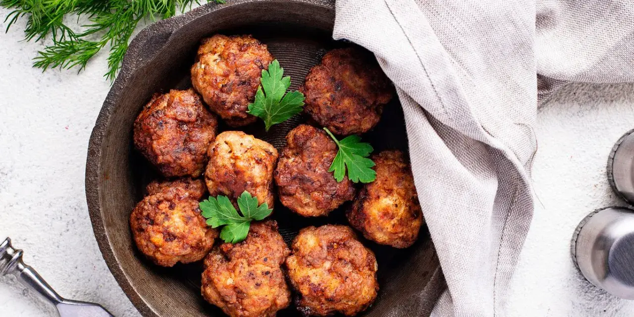Polpette senza uova dorate in padella, guarnite con prezzemolo fresco. Un piatto gustoso e leggero, pronto per essere gustato.