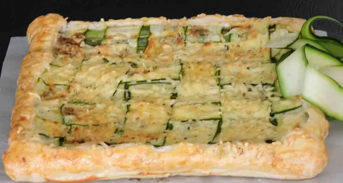 Torta salata con pasta sfoglia e zucchine a griglia, ricoperta di formaggio fuso e guarnita con fettine di zucchina fresca.