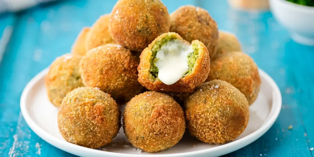 Pile di polpette di broccoli dorate e croccanti, una con il cuore filante di formaggio.