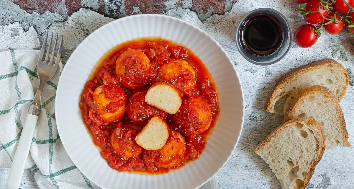 Polpette di ricotta al sugo, morbide e saporite, servite con pane casereccio e pomodorini freschi.