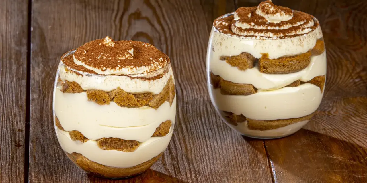 Due bicchieri di delizioso tiramisù senza uova, con strati di savoiardi e crema, spolverati di cacao.