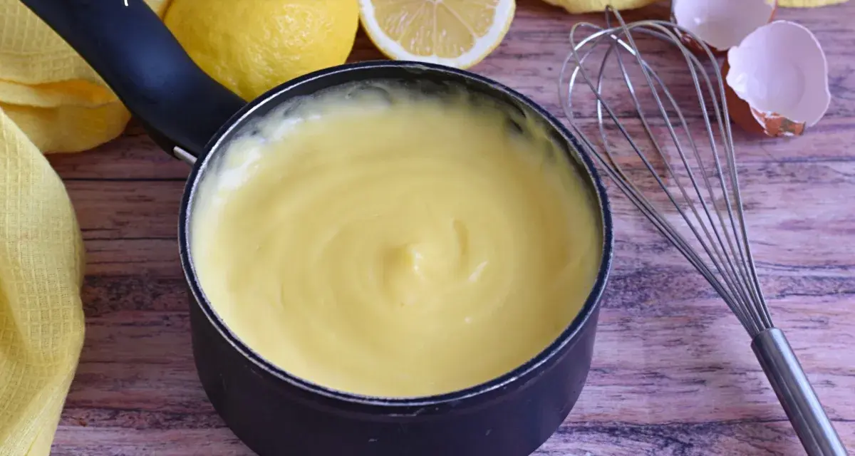Crema pasticcera con amido di mais, liscia e vellutata, pronta per farcire dolci. Accanto, limoni, frusta e gusci d'uovo.