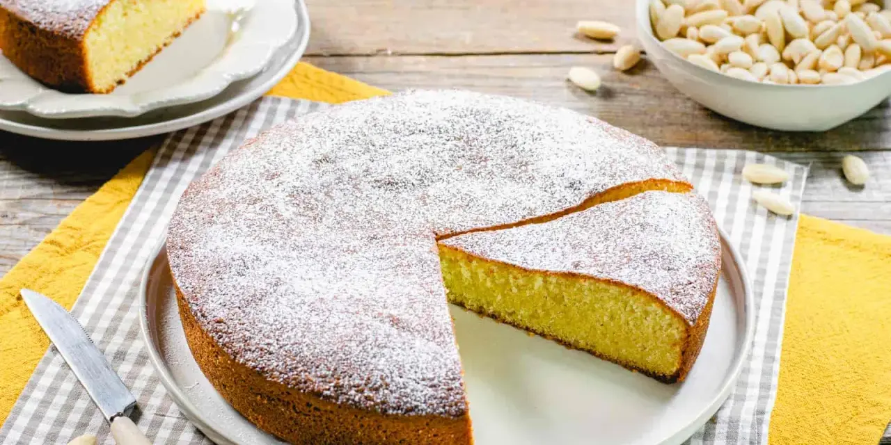 Torta soffice con farina di mandorle, spolverata di zucchero a velo. Un pezzo è già stato tagliato, pronto per essere gustato.
