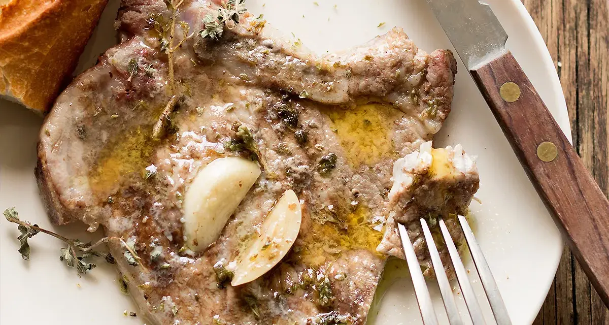 Succulente braciole di maiale cotte con aglio e erbe aromatiche, servite con pane croccante.