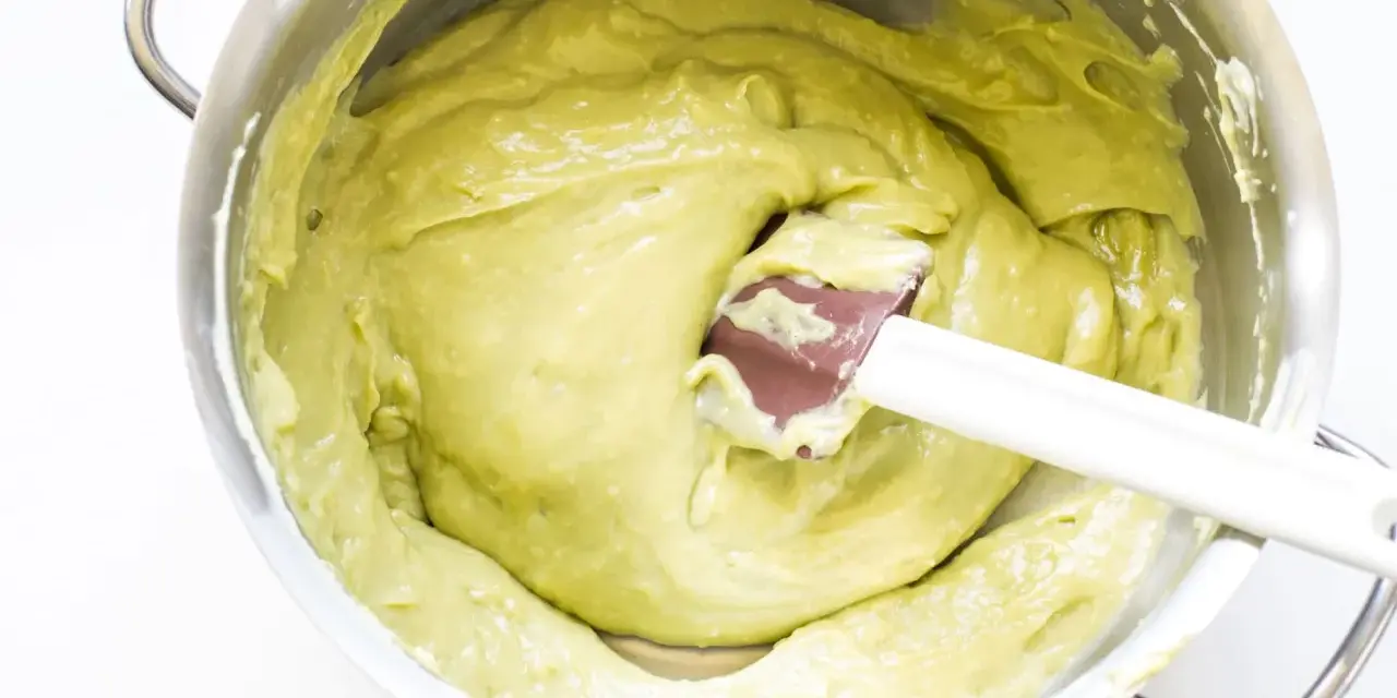 Una spatola mescola una densa crema al pistacchio in una ciotola d'acciaio.
