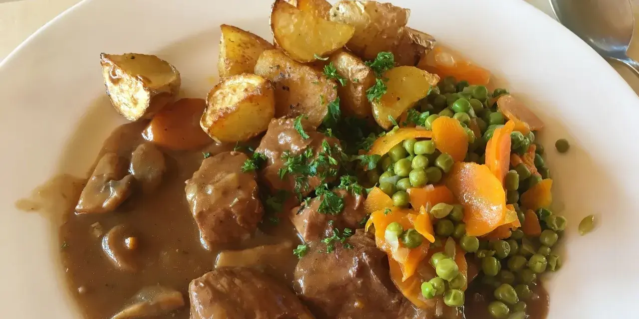 Un saporito spezzatino con piselli, carote e patate arrosto, guarnito con prezzemolo fresco.