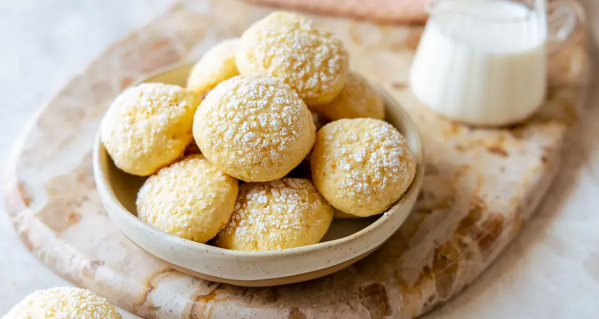Biscotti da inzuppo spolverati di zucchero a velo in una ciotola, pronti per essere gustati con un bicchierino di latte.