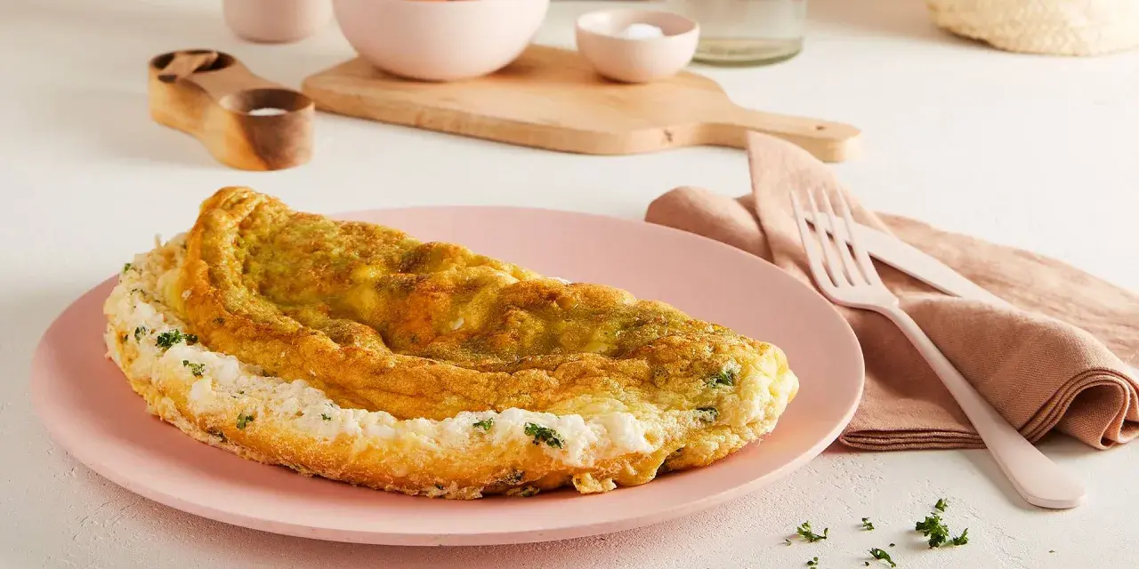 Frittata soffice e dorata, preparata in friggitrice ad aria, servita su un piatto rosa con erbe fresche.