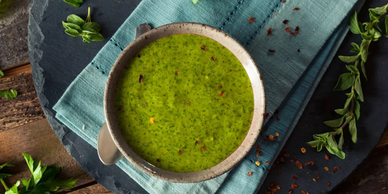Una ciotola di vibrante salsa verde senza uovo, guarnita con peperoncino rosso tritato e erbe fresche. Perfetta per accompagnare i tuoi piatti preferiti.