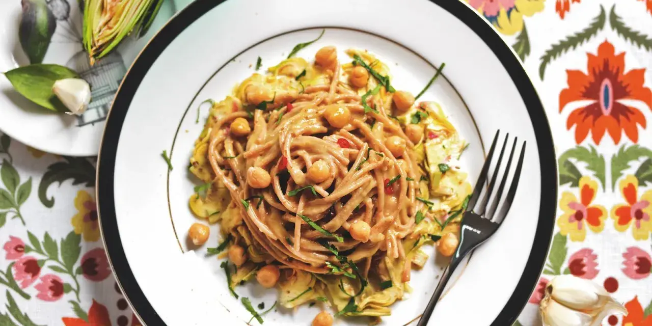 Un piatto invitante di pasta con carciofi alla siciliana, arricchito da ceci e erbe fresche, su un tovagliolo fiorito.