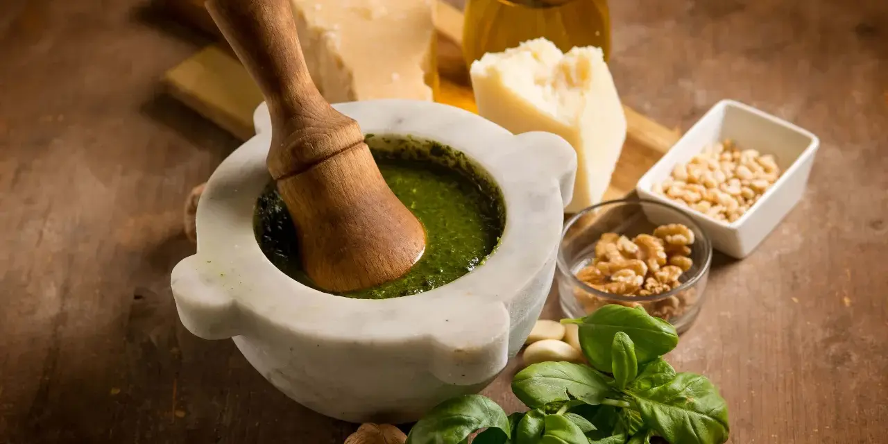 Mortaiolo in marmo con pestello in legno, basilico fresco, pinoli, noci, aglio, parmigiano e olio d'oliva, ingredienti per un autentico pesto di basilico.