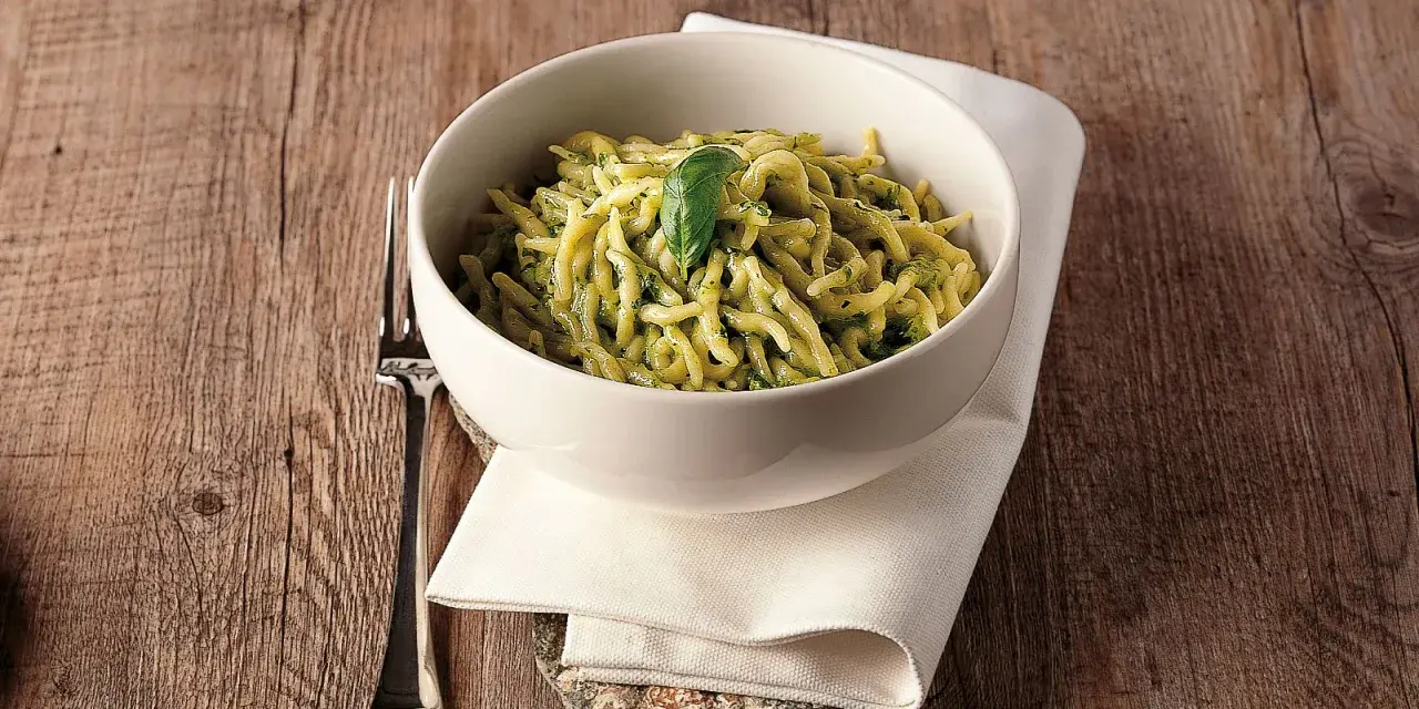 Un piatto invitante di trofie al pesto, guarnito con una foglia di basilico, su un tavolo di legno rustico.
