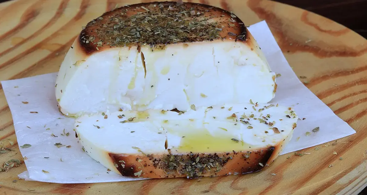 Ricotta al forno dorata e profumata con erbe aromatiche, servita su un tagliere di legno.