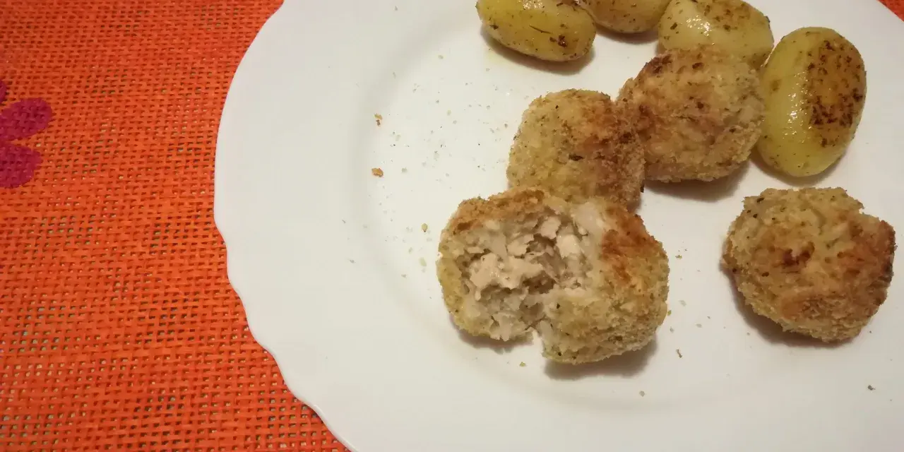Piatto con polpette di pollo dorate e patate novelle condite. Una polpetta è stata aperta, mostrando l'interno succulento.