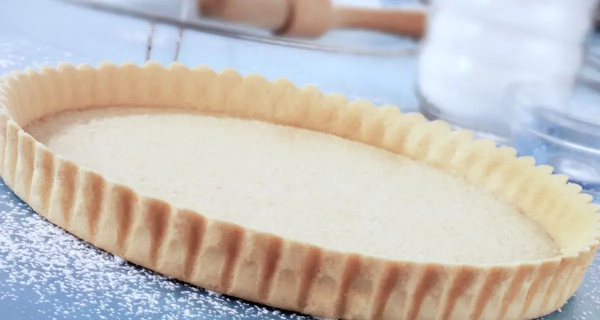 Base per crostata pronta, una deliziosa pasta frolla senza uova, cosparsa di zucchero a velo su un piano blu.