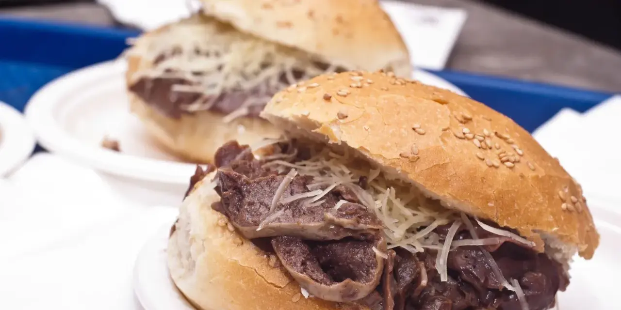 Panino con la milza, un classico street food siciliano, servito su un panino morbido con semi di sesamo e abbondante formaggio grattugiato.