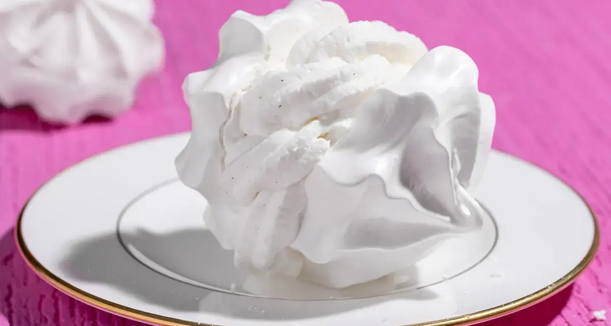 Dolci meringhe bianche, perfette per le tue ricette con albumi, su un piatto con bordo dorato, su sfondo fucsia.