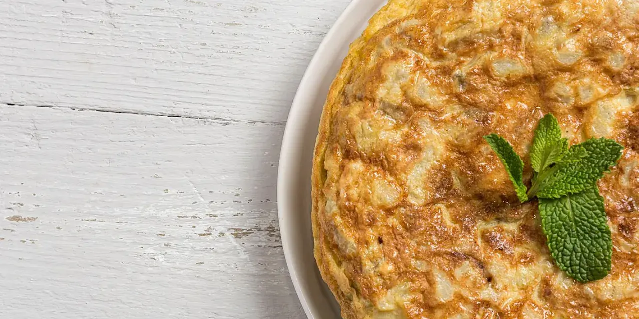 Frittata di cipolle dorata e soffice, guarnita con foglie di menta fresca, su un tavolo di legno bianco.