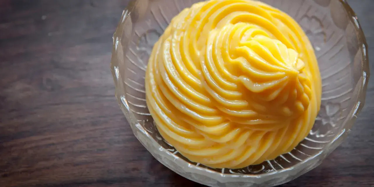 Crema pasticcera ricetta: una deliziosa crema gialla, liscia e lucida, servita in una ciotola di vetro trasparente con decori.