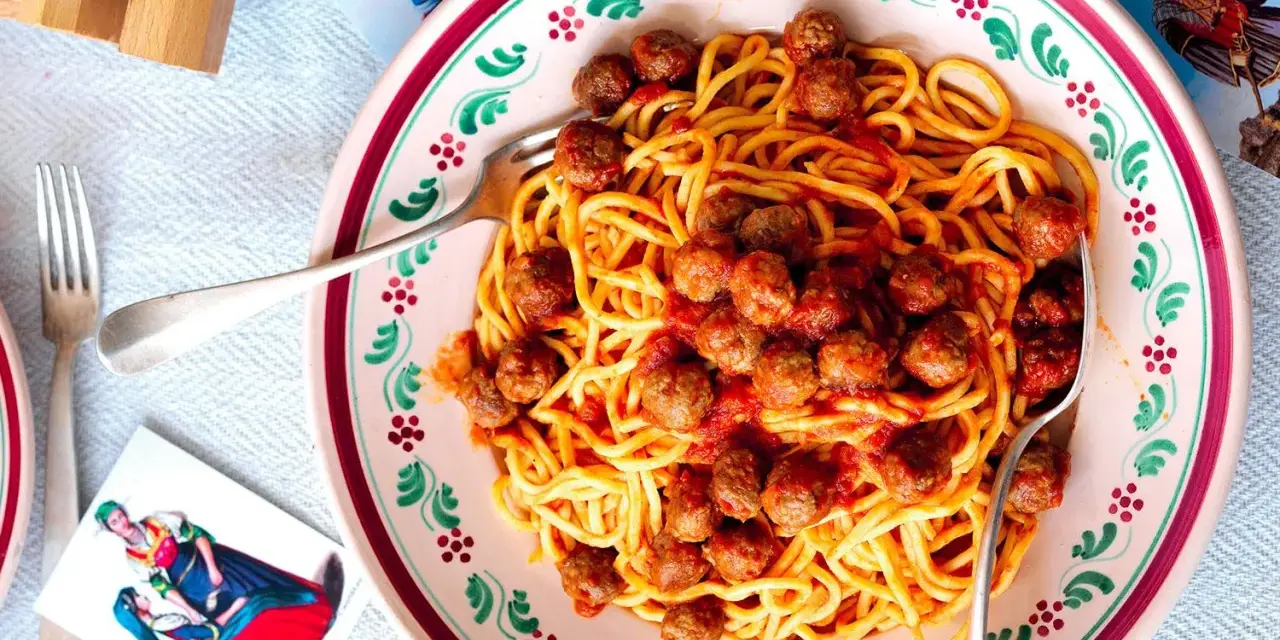 Un piatto di spaghetti alla chitarra con polpettine al sugo, serviti in un piatto decorato.
