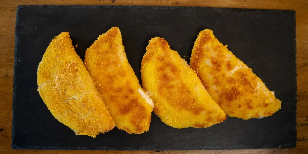 Quattro sofficini fatti in casa, dorati e croccanti, serviti su una pietra nera.