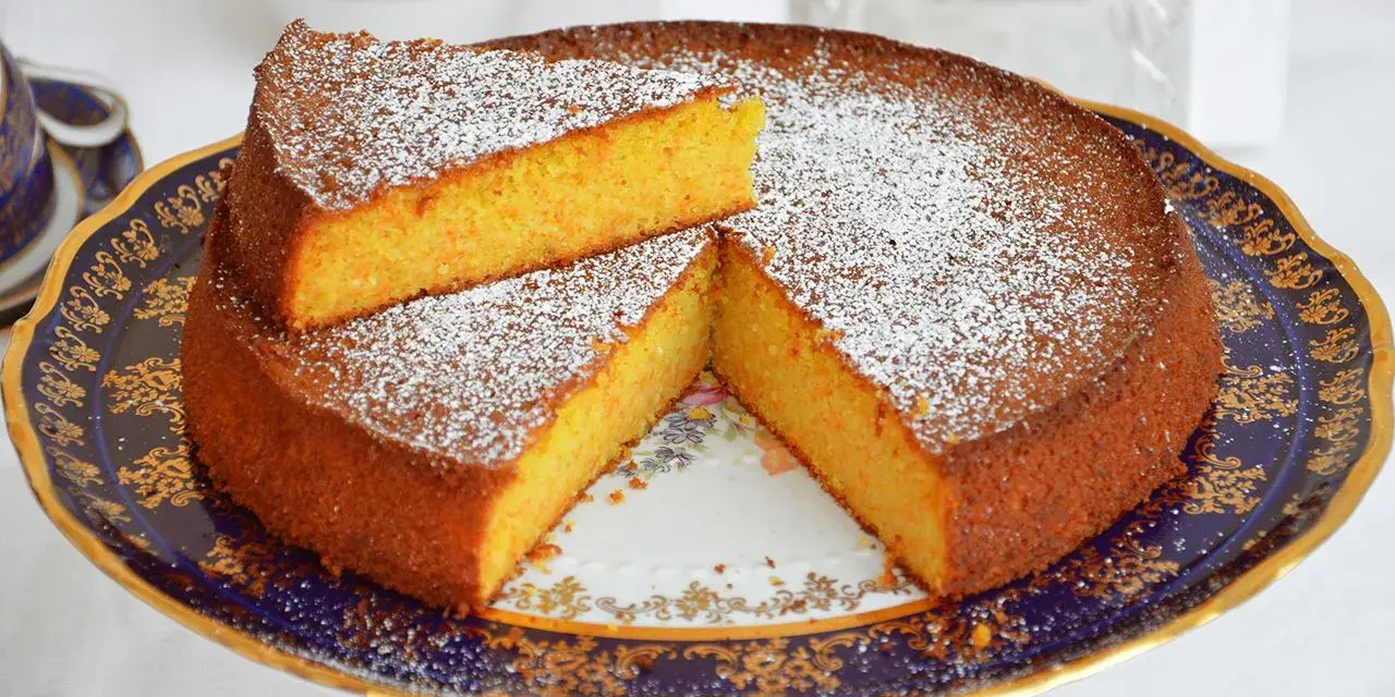 Deliziosa torta carote e mandorle, spolverata di zucchero a velo, servita su un elegante alzata.