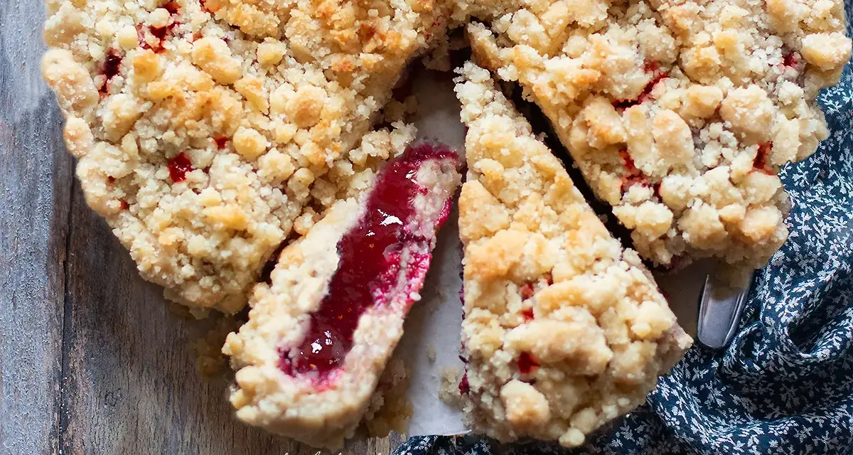 Torta con marmellata, con crosta friabile e ripieno rosso brillante. Una fetta mostra la consistenza succosa.