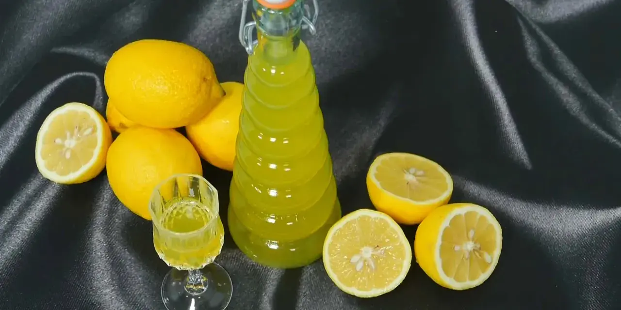 Limoncello fatto in casa: una bottiglia e un bicchierino di liquore giallo brillante, circondati da limoni freschi. La ricetta limoncello 1 litro alcool è pronta per essere gustata.
