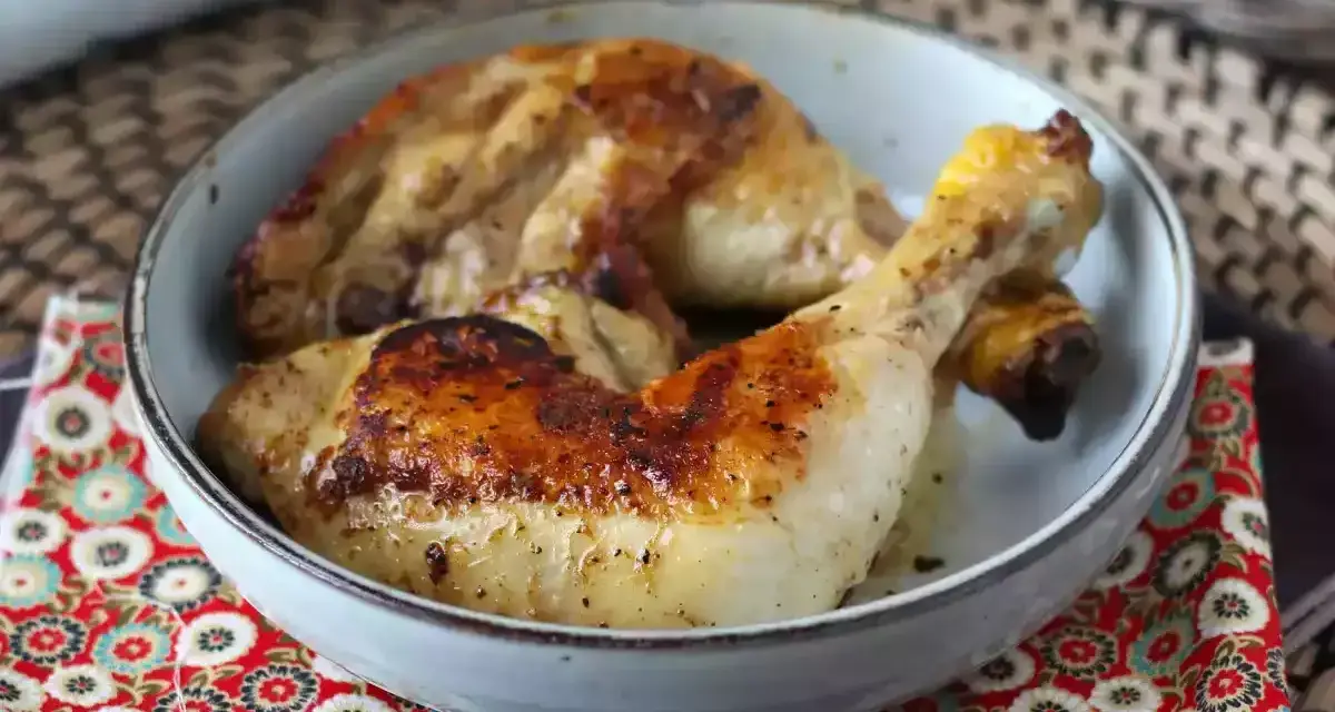 Cosce di pollo in padella, dorate e succulente, servite in una ciotola su un tovagliolo decorato.
