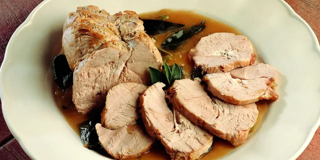Delizioso arrosto di tacchino affettato, servito in un sugo saporito con foglie di salvia su un piatto bianco.