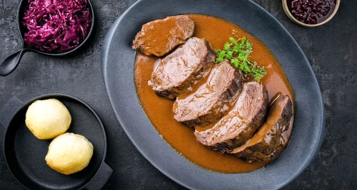 Fette fette di girello di vitello in salsa, accompagnate da cavolo rosso e canederli.