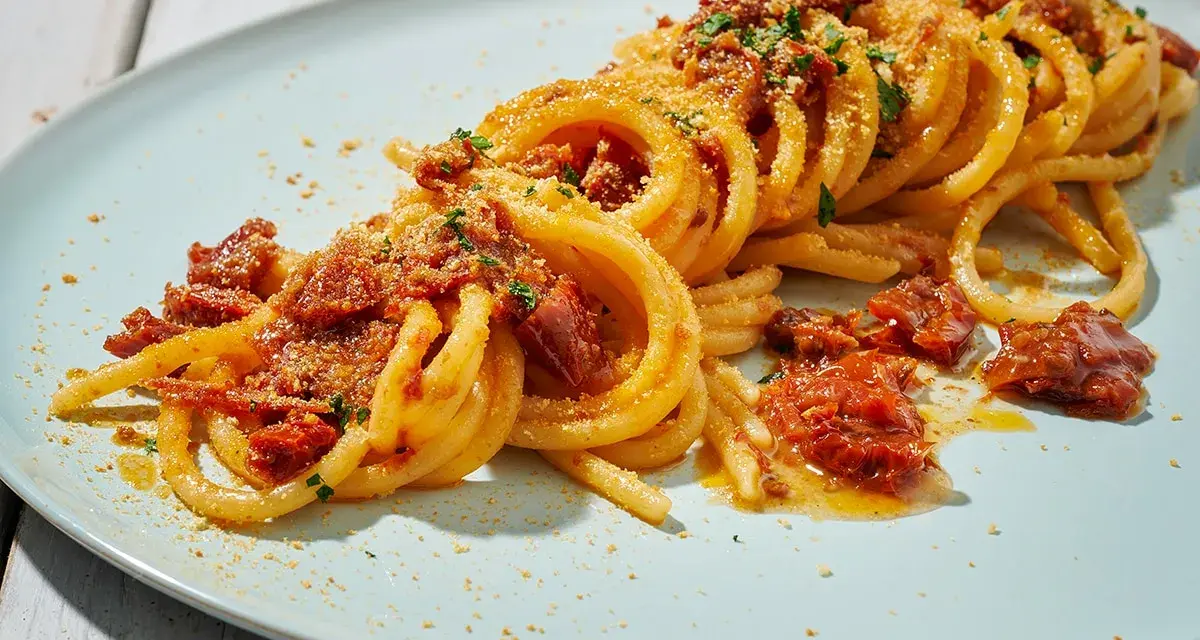 Spaghetti alla ghigliottina conditi con pomodorini secchi e pangrattato, un piatto invitante e saporito.