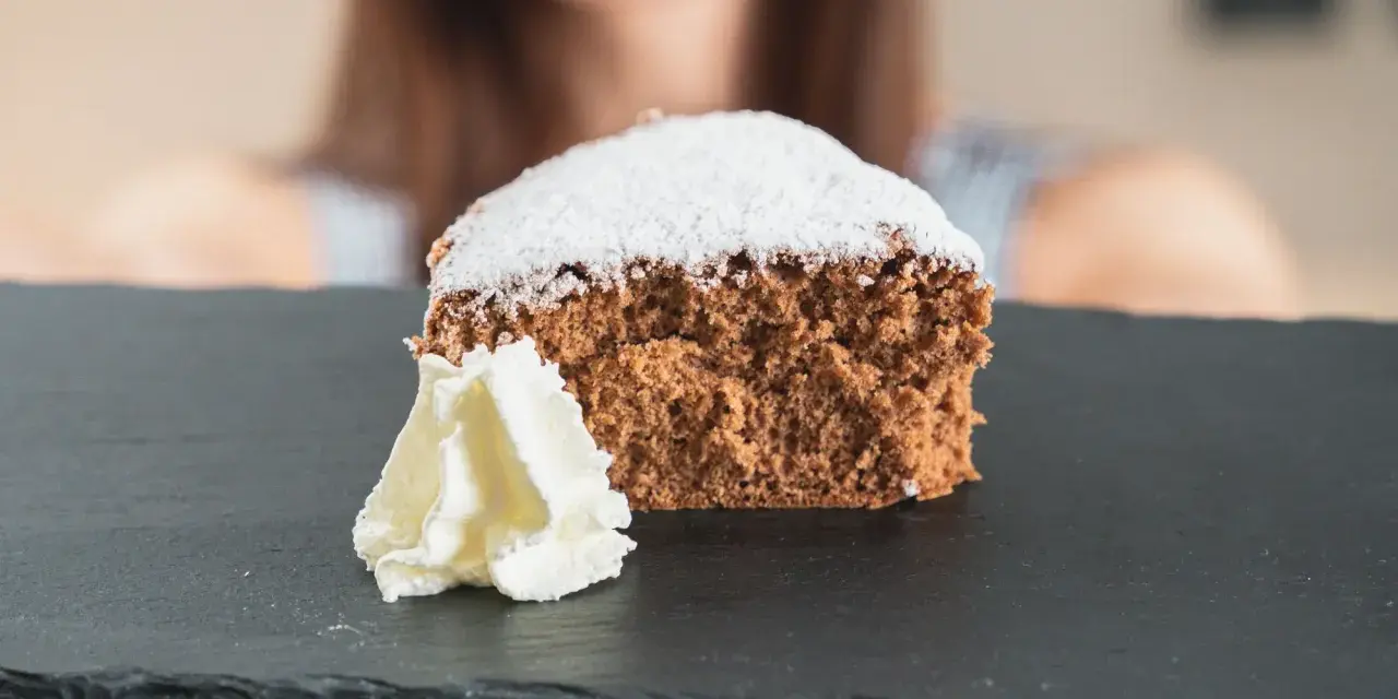 Una fetta di pan di spagna al cacao, soffice e spolverata di zucchero a velo, servita con panna montata su una lavagna scura.
