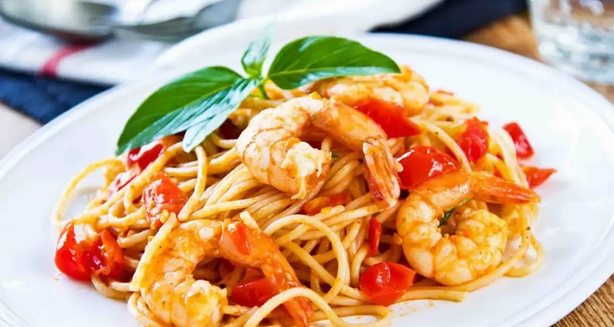 Un piatto invitante di spaghetti con gamberetti succulenti e pomodorini freschi, guarnito con basilico.
