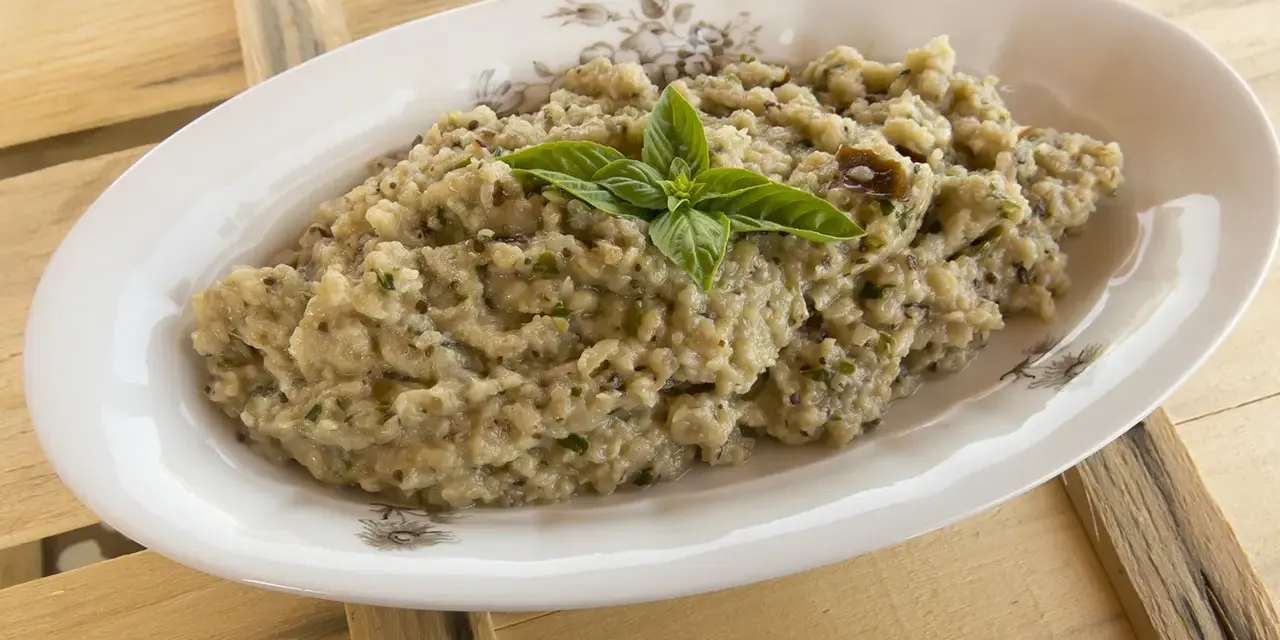Crema di melanzane rustica, guarnita con basilico fresco, servita in un piatto ovale su un tavolo di legno grezzo.