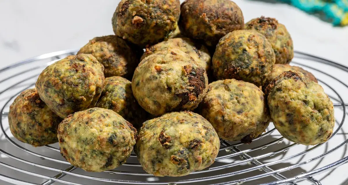 Pile di polpette ricotta e spinaci dorate e appetitose su una griglia metallica.