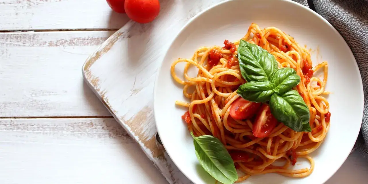 Spaghetti al sugo di pomodoro fresco, guarniti con basilico e pomodorini, su un piatto bianco.