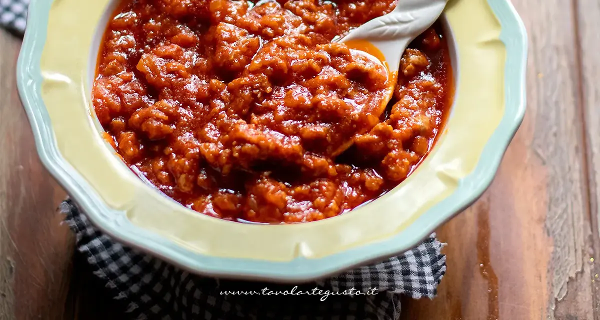 Un invitante sugo con salsiccia, denso e saporito, servito in una ciotola gialla con un cucchiaio decorato.