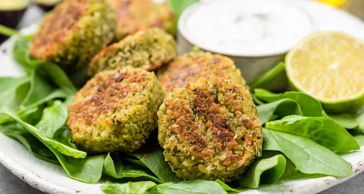 Deliziose polpette di spinaci dorate, servite su un letto di spinacini freschi con salsa e spicchi di lime.