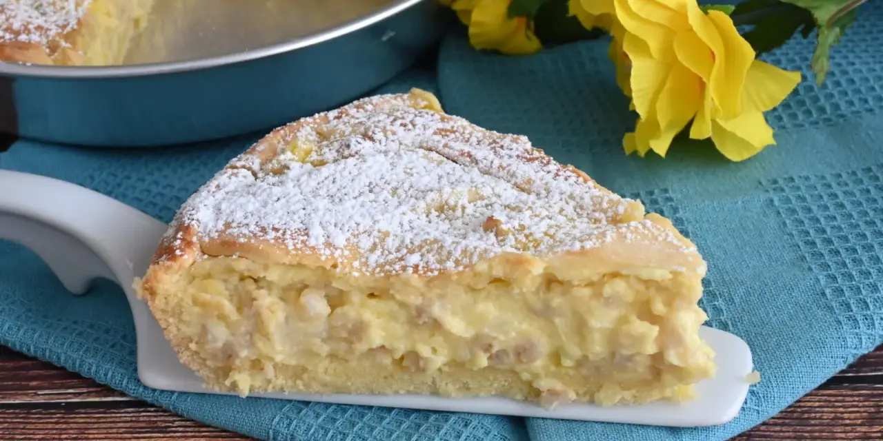 Una fetta di pastiera napoletana con crema pasticcera, cosparsa di zucchero a velo, su un piatto bianco, con fiori gialli sullo sfondo.