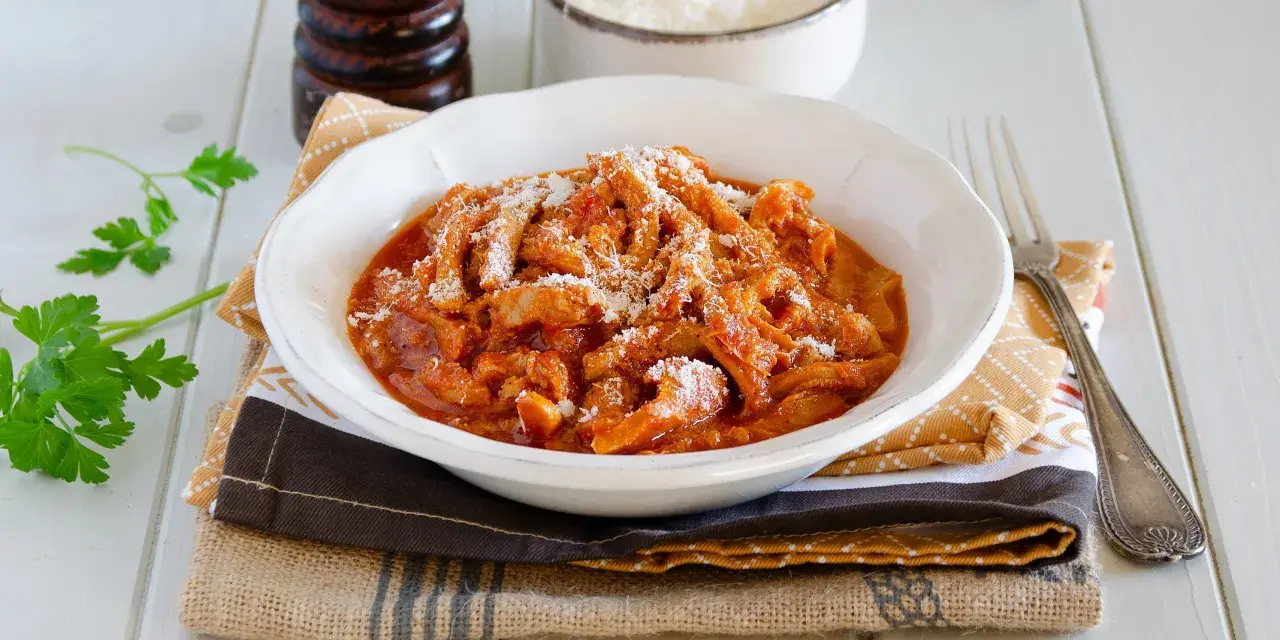 Un invitante piatto di trippa alla parmigiana, cosparso di formaggio grattugiato, pronto per essere gustato.