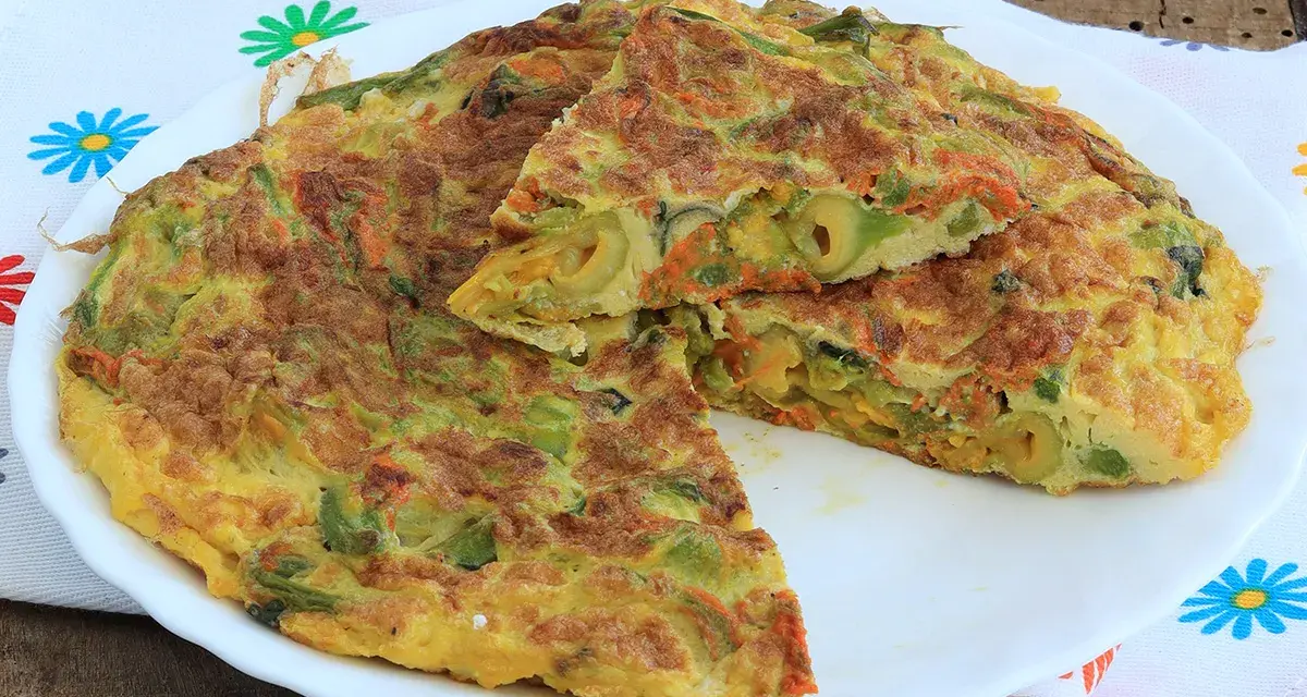 Frittata con fiori di zucca, carote e olive, tagliata a spicchi su un piatto bianco, con un tovagliolo fiorato sullo sfondo.