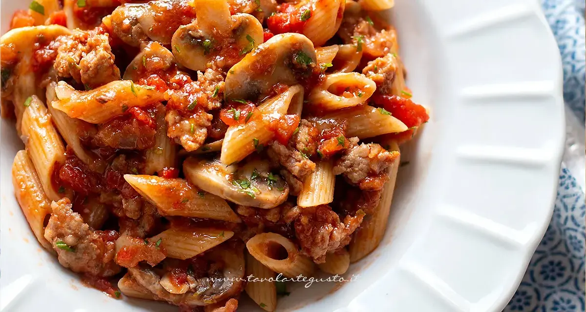 Piatto di pasta alla boscaiola con penne, funghi, salsiccia e pomodoro, condita con prezzemolo fresco.