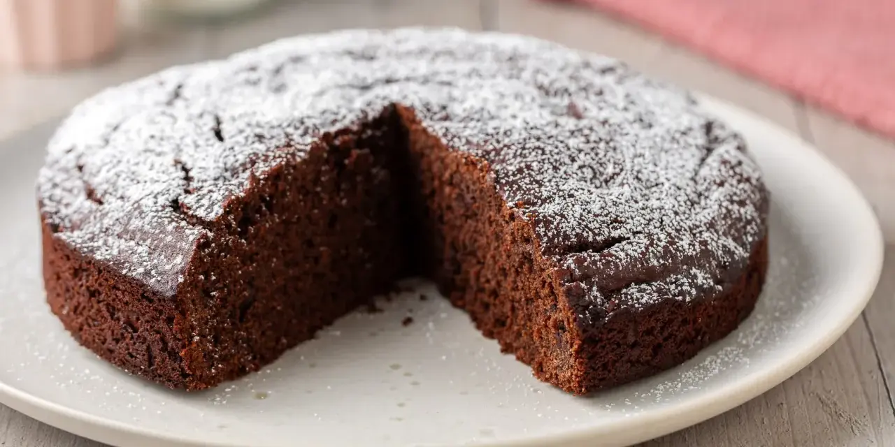 Una deliziosa torta al cioccolato, cosparsa di zucchero a velo, con una fetta mancante su un piatto bianco.