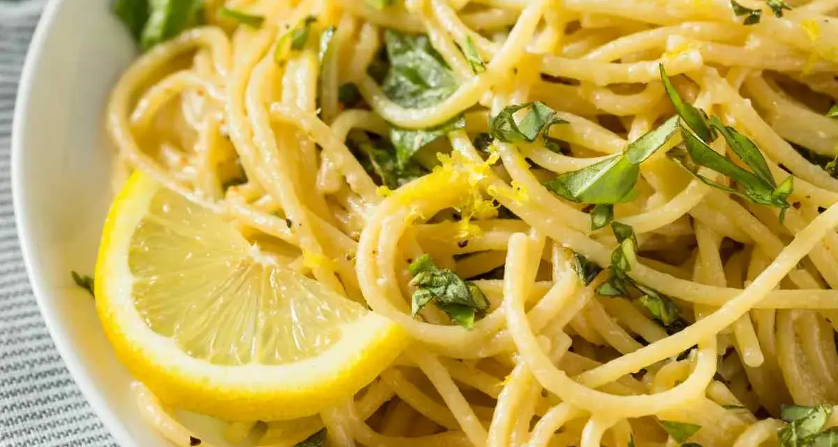 Un piatto invitante di spaghetti al limone, guarnito con scorza di limone e basilico fresco.
