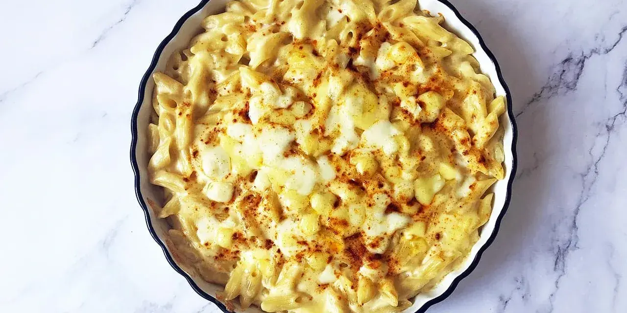 Piatto di mac and cheese fumante, con pasta penne cremosa e formaggio fuso, spolverato con paprika.